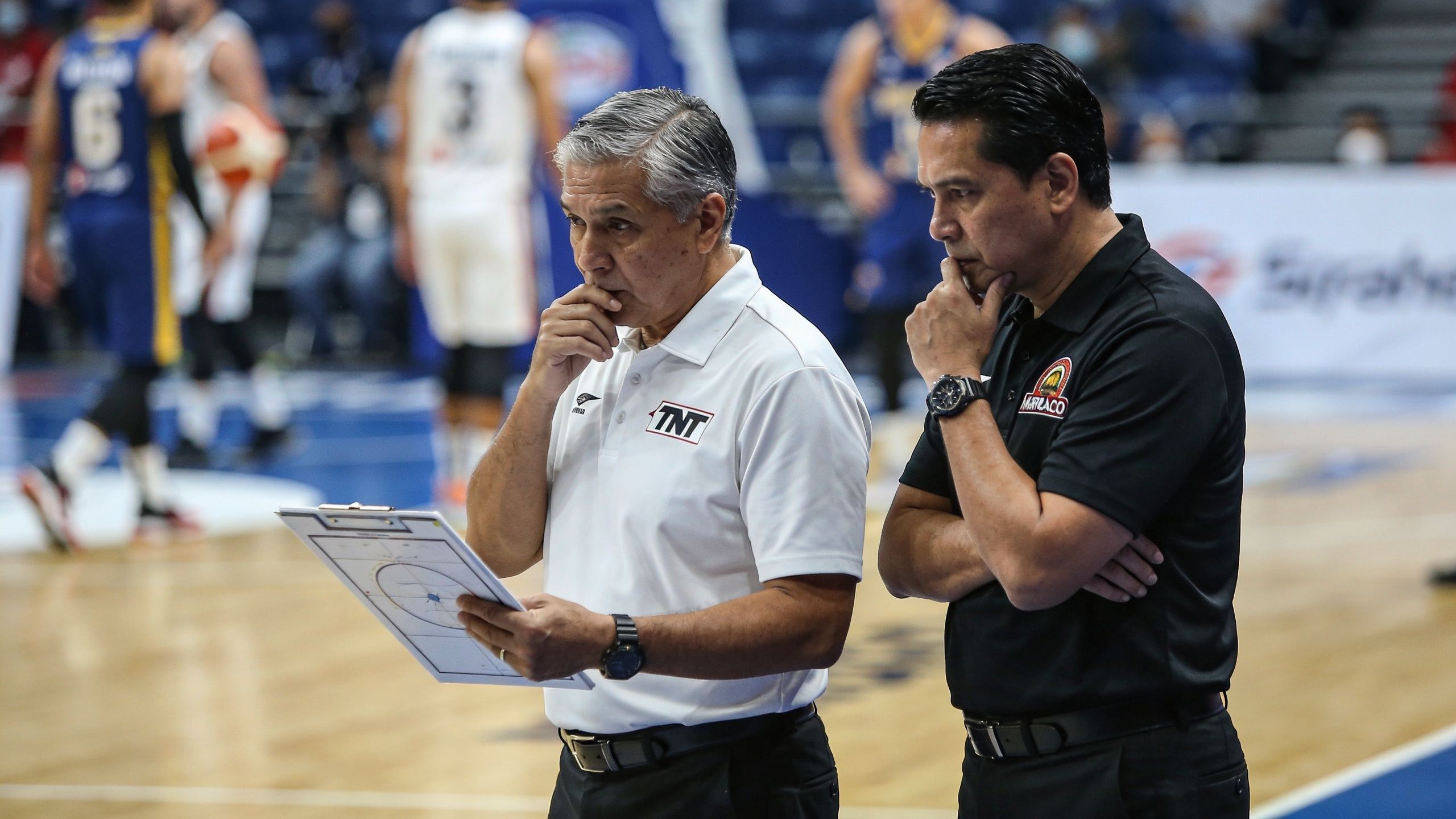 Two professional basketball coaches standing on the court, reviewing strategy on a tactical whiteboard during a game.