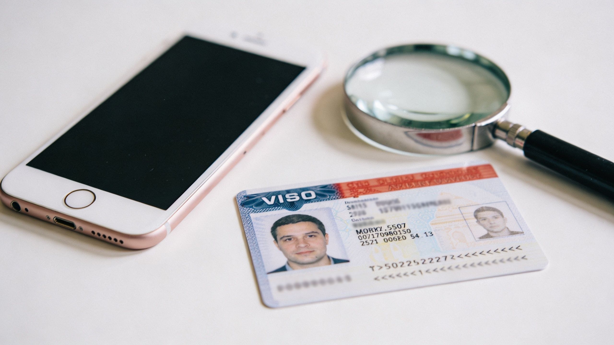 A smartphone, a magnifying glass, and a visa identification document on a clean white surface.