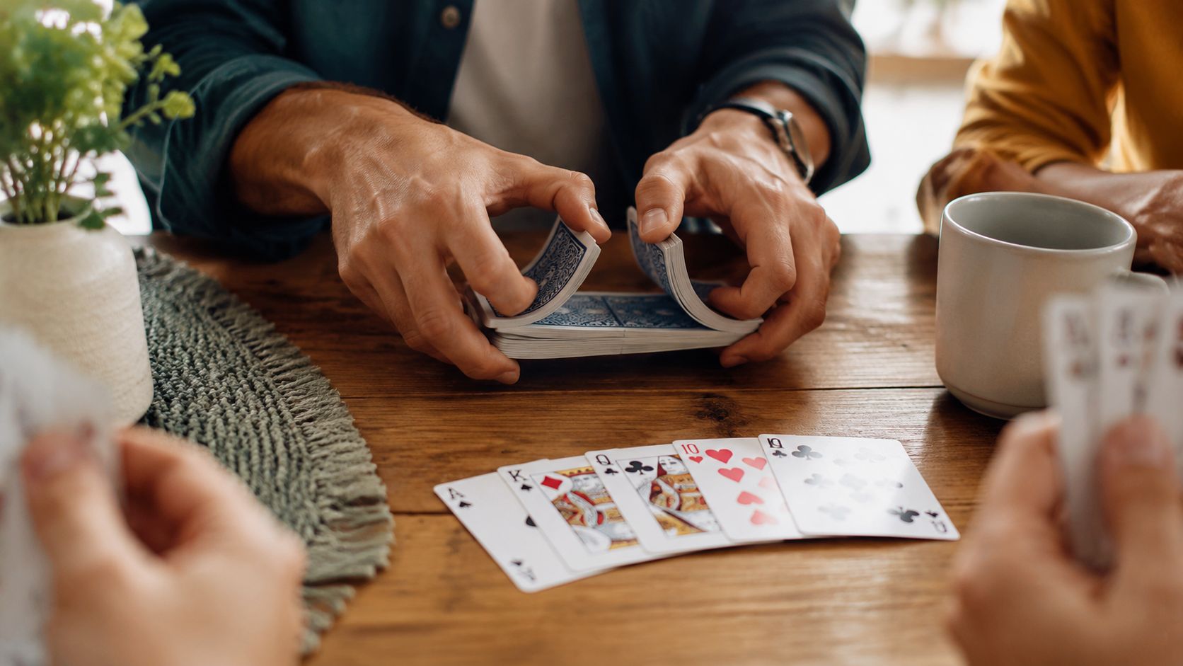 People sitting around a wooden table playing a card game and shuffling a deck of cards.